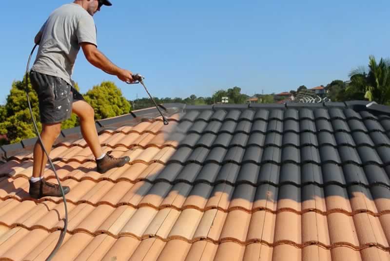 Worker applying coating to a tiled roof