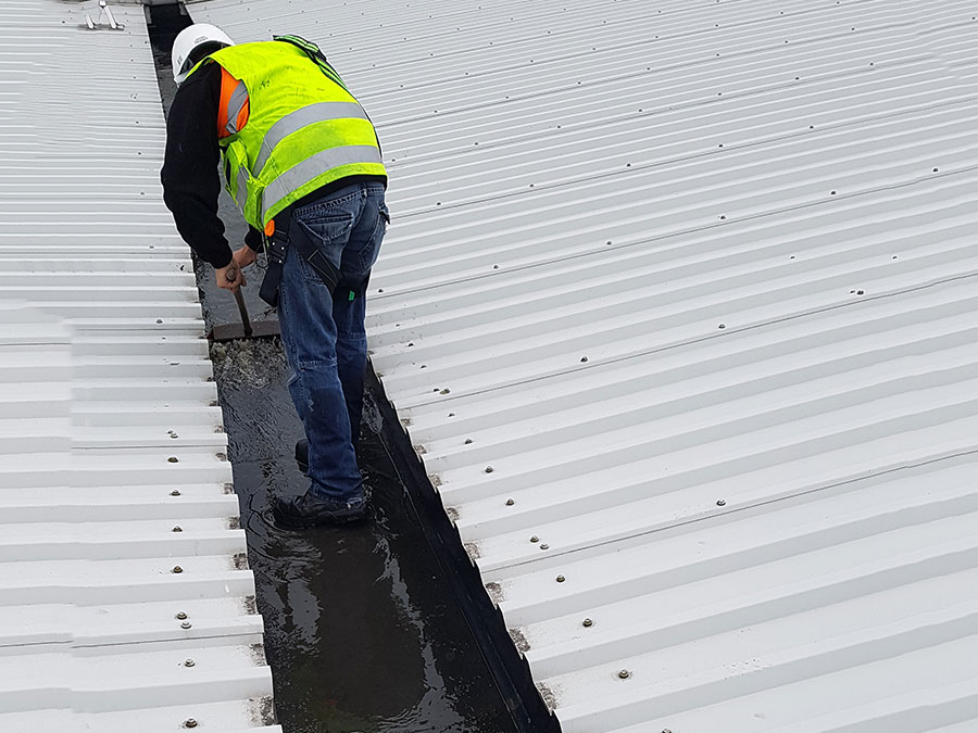 Worker inspecting a white metal warehouse roof for leak repairs